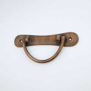 May include: A brass drawer pull with a curved handle and a rectangular base. The pull has a brushed finish and two small holes for mounting.