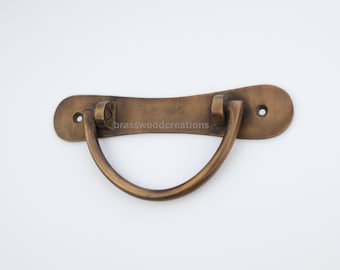 May include: A brass drawer pull with a curved handle and a rectangular base. The pull has a brushed finish and two small holes for mounting.