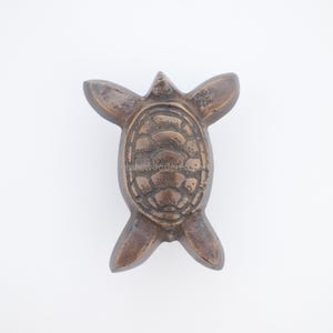 Pu&ograve; includere: Statuetta a forma di tartaruga color bronzo con pinne distese e un motivo a guscio dettagliato. La tartaruga &egrave; posizionata su uno sfondo bianco. La statuetta &egrave; un oggetto decorativo.