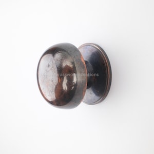 Op de afbeelding: Een bronzen deurknop in vintage stijl, met een gladde, ronde handgreep en een cirkelvormige achterplaat. De knop heeft een reflecterend oppervlak, wat duidt op een gepolijste afwerking. Deurbeslag.