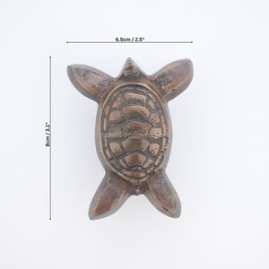 Pu&ograve; includere: Statuetta a forma di tartaruga color bronzo, larga 6,5 cm e lunga 8 cm. La tartaruga ha un motivo a guscio dettagliato e pinne distese. La statuetta &egrave; su sfondo bianco.