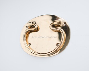 May include: A gold-toned oval-shaped cabinet pull with a decorative loop handle. The pull has four screw holes and the text "brasswoodcreations" is visible on the plate.