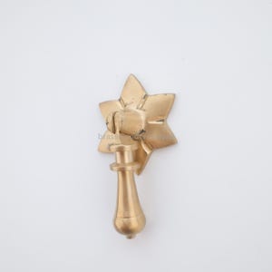 May include: A gold-coloured star-shaped drawer pull with a teardrop-shaped handle. The hardware has a vintage aesthetic. The text "brass wonder" is visible on the pull.