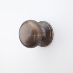 Op de afbeelding: Een bronzen deurknop met een ronde handgreep en een cirkelvormige basis. De knop heeft een gladde, gepolijste afwerking en staat tegen een witte achtergrond. De hardware is waarschijnlijk voor een deur of kast.