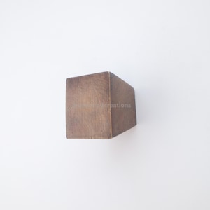 May include: A solid, rectangular wooden block with a natural brown finish. The block is positioned at an angle against a white background, showcasing its geometric shape and wood grain texture. The product is a cube.
