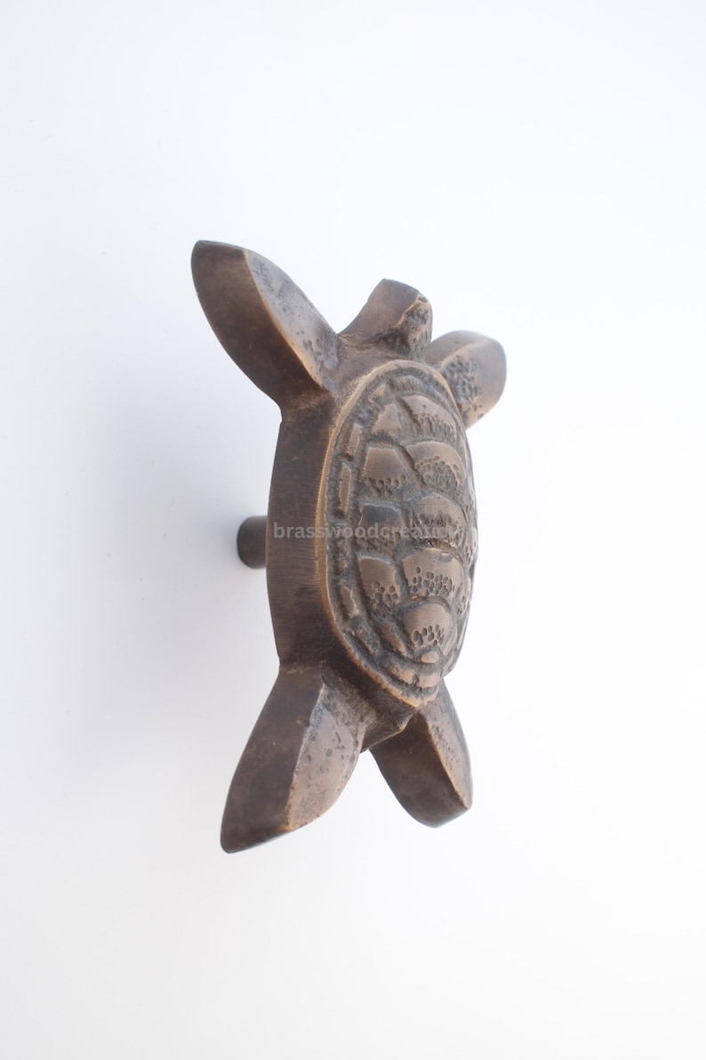 Pu&ograve; includere: Pomello per armadio a forma di tartaruga color bronzo. Il pomello presenta un design dettagliato di tartaruga con un guscio strutturato e braccia e gambe a forma di pinna. Il pomello &egrave; montato su una piccola base rotonda.