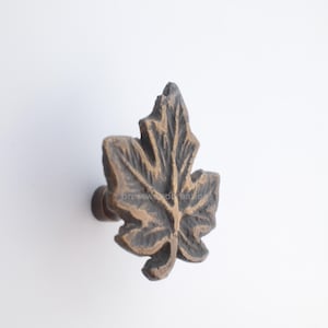 May include: A bronze-coloured leaf-shaped cabinet knob. The knob has a detailed leaf design with visible veins and a dark brown finish. The text "brasswood creations" is visible on the knob.