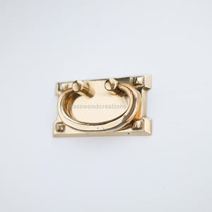 May include: A gold-toned metal cabinet pull with a rectangular base and a curved handle.