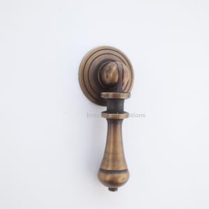 May include: Antique brass cabinet pull with a round backplate and a decorative handle. The pull has a classic design with a detailed, aged finish. The product is a hardware item.