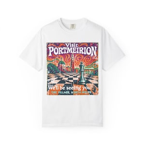 May include: White t-shirt featuring a vintage-style graphic promoting Portmeirion, North Wales. The design includes the text "Visit Portmeirion" and "We'll be seeing you!" with a chess-themed illustration in shades of orange, purple, and green.
