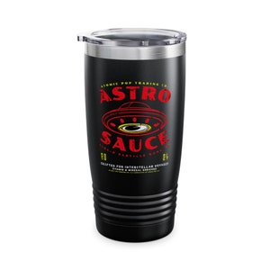 May include: Black stainless steel tumbler with a red and white graphic of a UFO and the text "ATOMIC POP TRADING CO. ASTRO SAUCE LIQUID PARTICLE BOOSTER 20 24 CRAFTED FOR INTERSTELLAR VOYAGES VITAMIN & MINERAL ENRICHED".