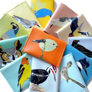 an assortment of brightly colored vegan leather wallets, each with a different illustration of a US native bird species