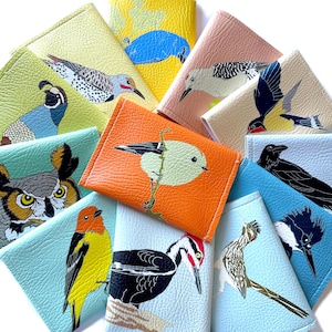 an assortment of brightly colored vegan leather wallets, each with a different illustration of a US native bird species