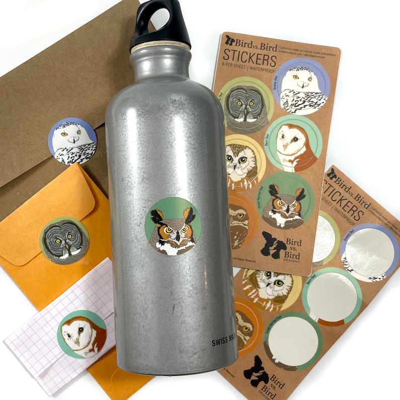May include: A silver water bottle with a sticker of an owl on it. The sticker is part of a set of stickers featuring different types of owls. The stickers are waterproof and come in a sheet of 8. The text on the sticker sheet reads "Bird vs Bird Stickers".