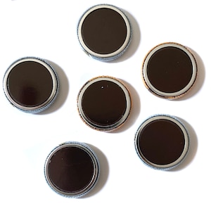 May include: Six round, silver-rimmed, black button pins with a white backing.
