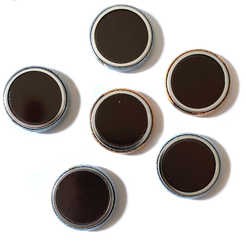 May include: Six round, silver-rimmed, black button pins with a white backing.