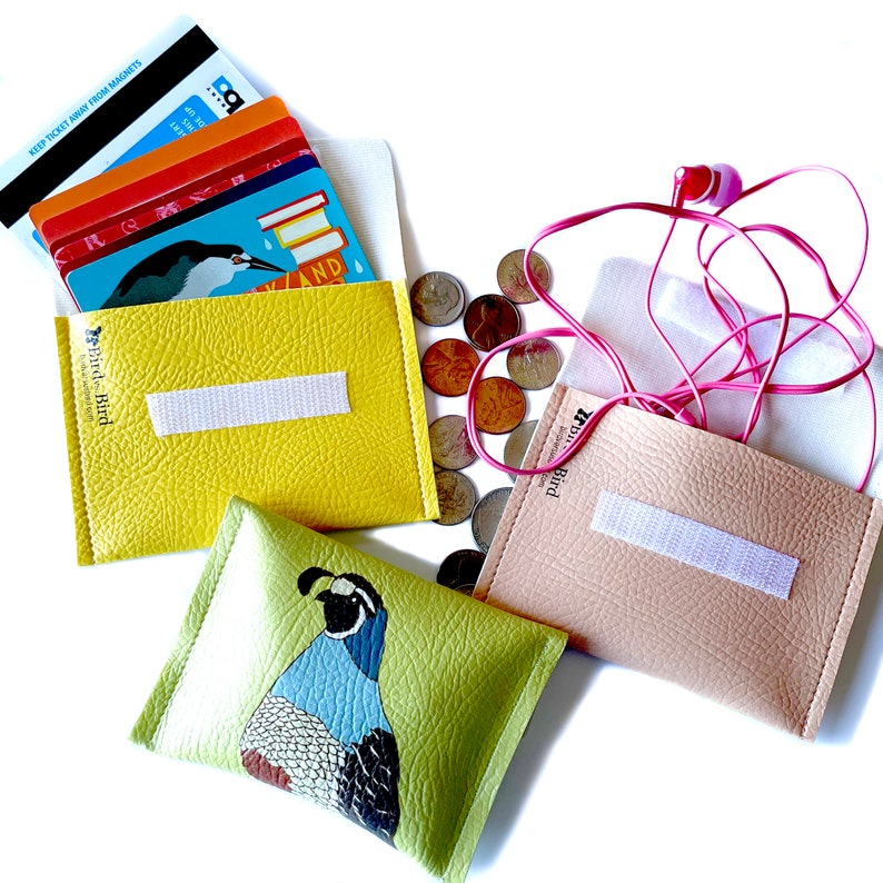 three vegan leather wallets on a white background. Two wallets are open to show velcro closure and usage. A yellow wallet holds library and transit cards. A pink wallet holds wire earbuds. A green wallet with a california quail design is also shown