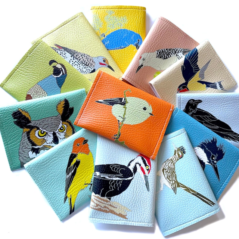 an assortment of brightly colored vegan leather wallets, each with a different illustration of a US native bird species