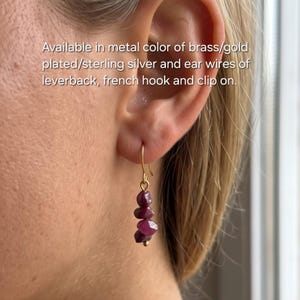 Peut inclure: Une boucle d'oreille dorée composée de trois petites perles de pierre brute rose foncé irrégulières suspendues à un crochet métallique fin. Le texte indique : Available in metal color of brass/gold plated/sterling silver and ear wires of leverback, french hook and clip on.