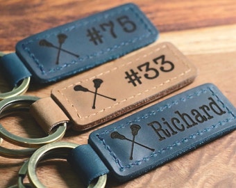 May include: Three leather keychains with a lacrosse stick design. The keychains are blue, brown, and tan. The blue keychain has the name "Richard" and the number "75". The brown keychain has the number "33".