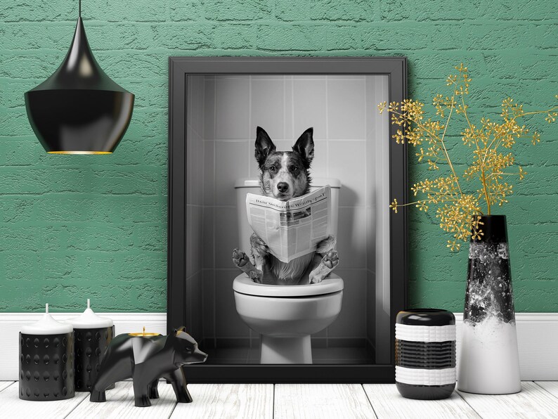 May include: A black and white photo of a dog sitting on a toilet, reading a newspaper. The dog is wearing a collar and has a surprised expression on its face. The photo is framed in a black frame and hanging on a green wall.