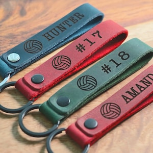 Könnte beinhalten: Vier Leder-Schlüsselanhänger mit einem Volleyball-Design und personalisiertem Text. Die Schlüsselanhänger sind in Blau, Rot, Grün und Rot. Der Text auf den Schlüsselanhängern lautet "Hunter", "#17", "#18" und "Amanda".