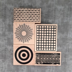 May include: Four wooden stamps with black and white geometric designs. The stamps feature a circle with radiating lines, a grid pattern, a target, and a repeating pattern of squares.