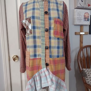 Puede incluir: Una camisa de cuadros patchwork con un diseño único. La camisa presenta una mezcla de estampados de cuadros en varios colores, incluyendo amarillo, azul, naranja y rojo. Tiene botones negros grandes y un dobladillo con volantes. Las mangas son de cuadros burdeos.