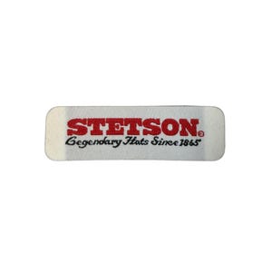 May include: A rectangular label with rounded corners. The word "STETSON" is printed in bold, red letters. Below, in smaller, cursive red letters, it reads "Legendary Hats Since 1865". The label is on a white background.