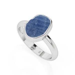 May include: A silver ring featuring a large, irregular-shaped blue gemstone. The gemstone is set in a polished silver band. The ring is shown against a white background, highlighting its design and color.