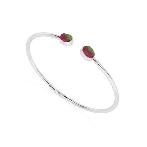 May include: A silver-colored open cuff bracelet with a raw, natural watermelon tourmaline gemstone at each end. The gemstones display a mix of pink and green hues, set against the polished metal.