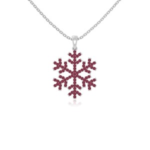 May include: A silver-toned necklace featuring a snowflake pendant. The pendant is composed of numerous small, round, burgundy-colored stones arranged in a snowflake design. The necklace chain is delicate and silver.