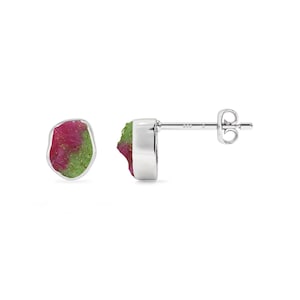 May include: A pair of stud earrings featuring raw, irregular-shaped ruby and zoisite stones set in polished sterling silver. Each earring displays a vibrant mix of deep pink and green mineral textures, complete with silver posts and butterfly backs.