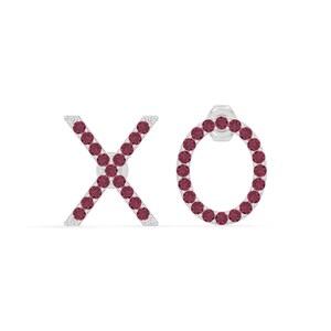 May include: A pair of stud earrings spelling out "XO". The letters are formed with small, round, dark red gemstones set in a silver metal. The earrings are displayed against a white background.