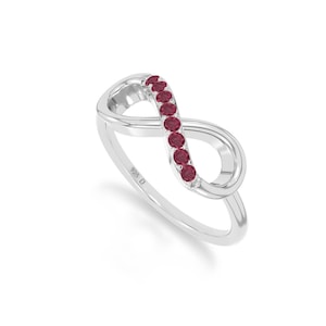 May include: A silver infinity ring with a row of round, red gemstones. The ring is made of polished metal and features the inscription "925 D" on the band. The infinity symbol is a continuous loop.