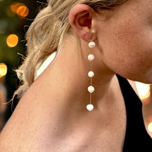 May include: A long, delicate pearl earring with five white pearls hanging from a thin gold chain.