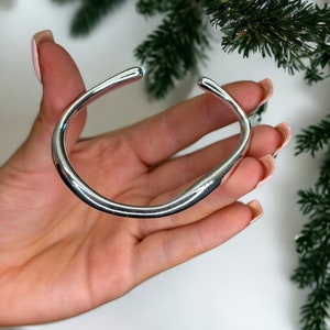 May include: A silver bangle bracelet with a smooth, rounded design.