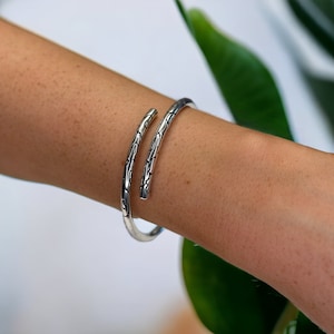 Puede incluir: Un brazalete de plata con un diseño texturizado en espiral. El brazalete es abierto y ajustable.