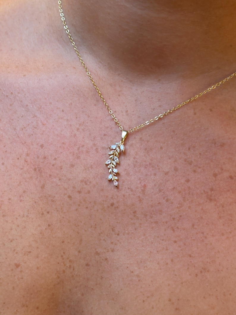 Pu&ograve; includere: Una collana con catena dorata con un delicato ciondolo a forma di ramo con piccoli cristalli trasparenti.