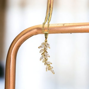 Pu&ograve; includere: Una collana d'oro con un delicato ciondolo a forma di foglia con pietre di zircone cubico trasparenti.