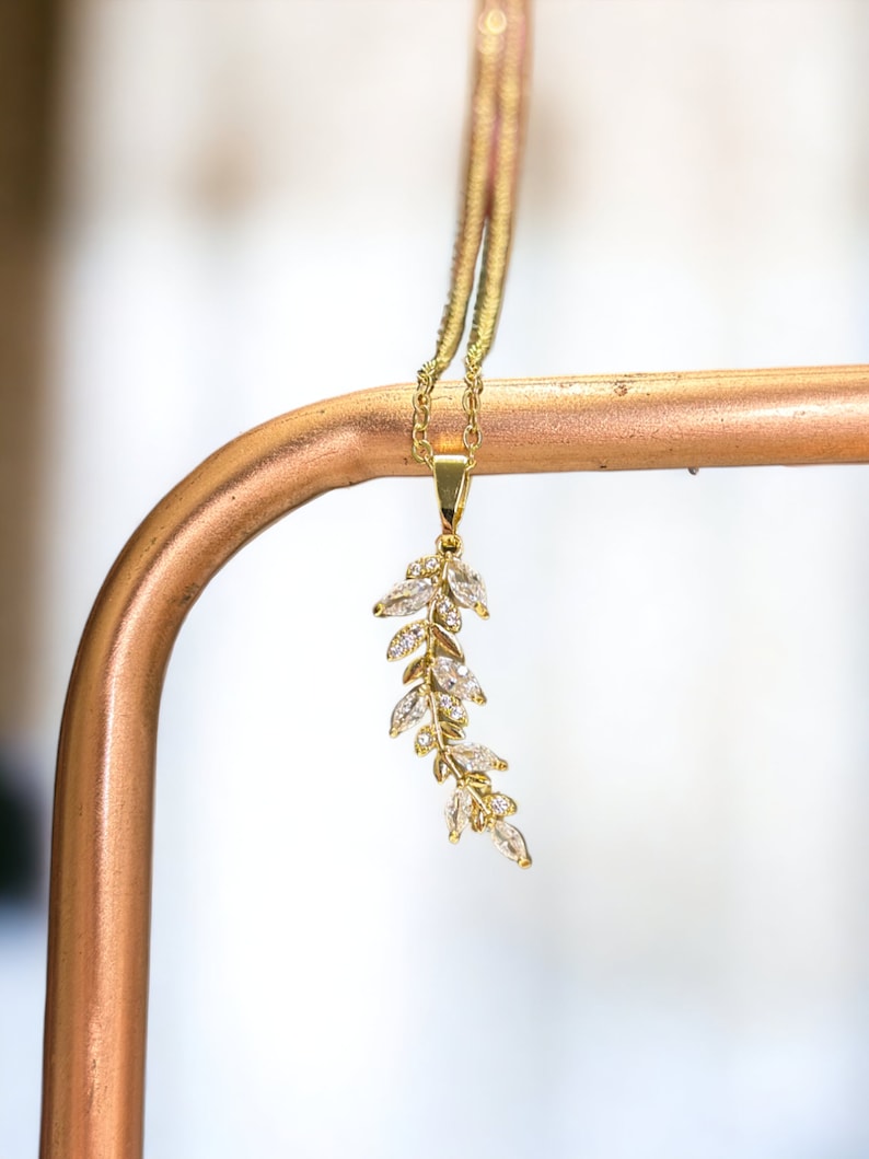 Pu&ograve; includere: Una collana d'oro con un delicato ciondolo a forma di foglia con pietre di zircone cubico trasparenti.