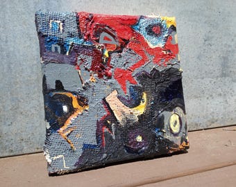 May include: Abstract painting on canvas with a textured surface. The artwork features a mix of colors, including red, gray, black, blue, and yellow. The painting has a rough, layered appearance, with visible brushstrokes and a raw, unfinished edge.
