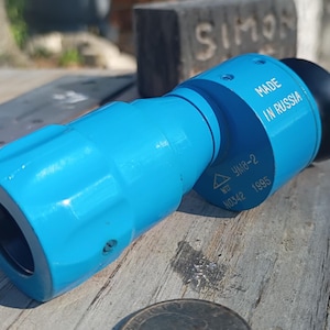 Puede incluir: Un objeto cilíndrico azul con una tapa negra, etiquetado como "MADE IN RUSSIA". El objeto tiene un diseño estriado y parece estar hecho de metal o plástico duradero. Se ven textos y marcas adicionales.