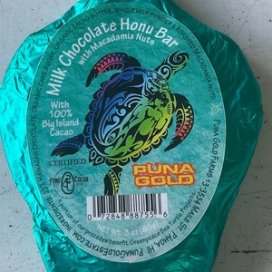May include: A turquoise foil-wrapped chocolate bar with a green sea turtle design. The bar is labeled "Milk Chocolate Honu Bar with Macadamia Nuts" and "Puna Gold". The bar is 3 ounces.