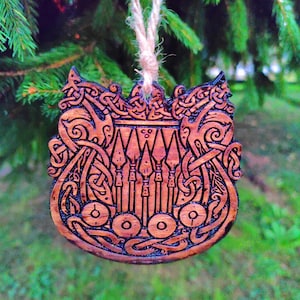May include: A wooden ornament featuring intricate carvings of a shield with a Celtic knot design. The ornament is brown and has a string loop for hanging.