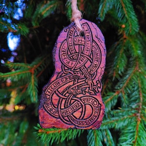 May include: A wooden Christmas bauble featuring a carved knotwork design and runes. The bauble is painted in shades of brown and red.