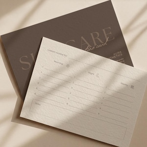 Peut inclure: Une carte de routine de soins de la peau avec le texte "SKINCARE fine card" et "custom routine for" imprimé dessus. La carte comporte des sections pour les routines du matin, du soir et hebdomadaires. La carte est beige clair avec une carte gris foncé derrière.