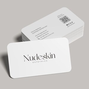May include: A stack of white business cards with rounded corners. The top card displays the text "Nudeskin Esthetics" in a stylish font. Additional cards show contact information, a QR code, and social media handles.