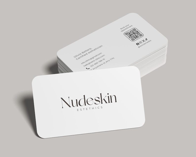 May include: A stack of white business cards with rounded corners. The top card displays the text "Nudeskin Esthetics" in a stylish font. Additional cards show contact information, a QR code, and social media handles.