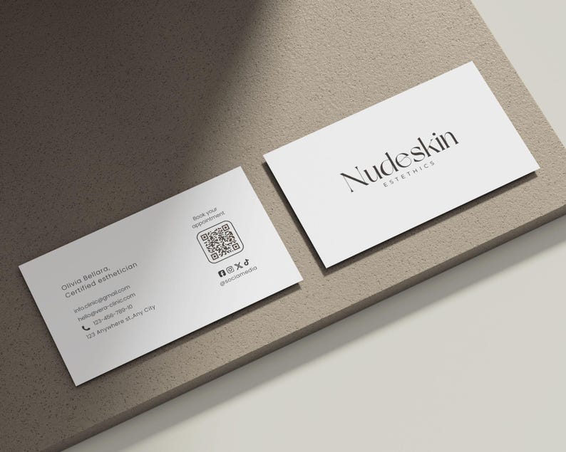 May include: Two white business cards with the text "Nudeskin Esthetics" and contact information. One card displays the business name, while the other includes a QR code and social media handles. The cards are on a neutral-toned surface.